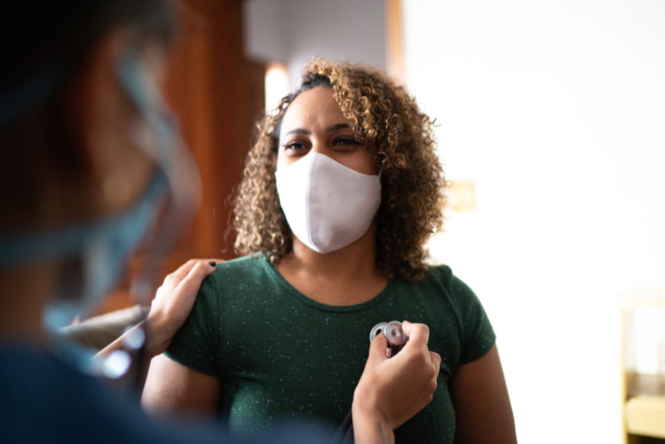woman wearing mask getting heart check with stethoscope 