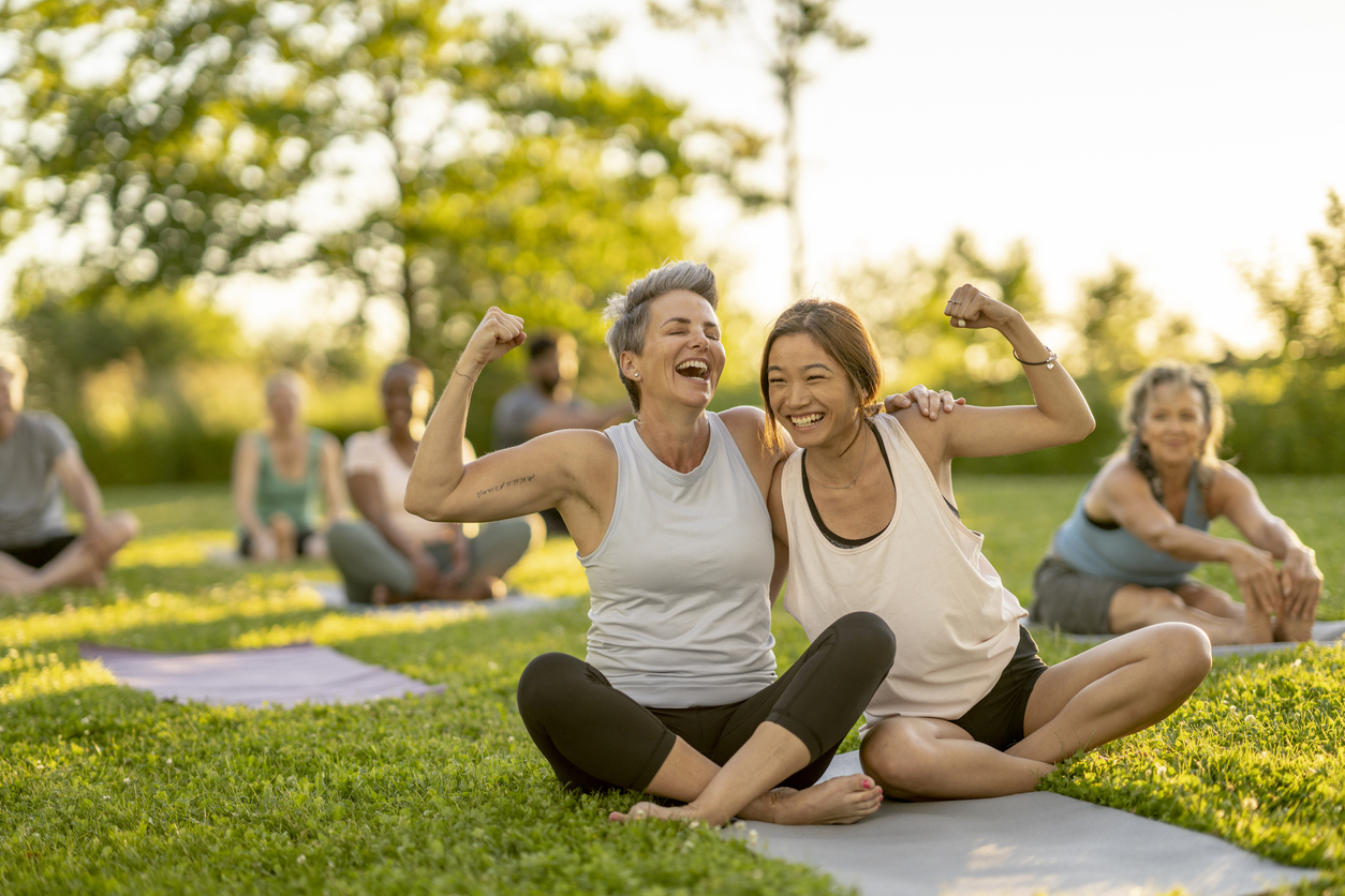 Two people smiling and showing their biceps at an outdoor exercise class