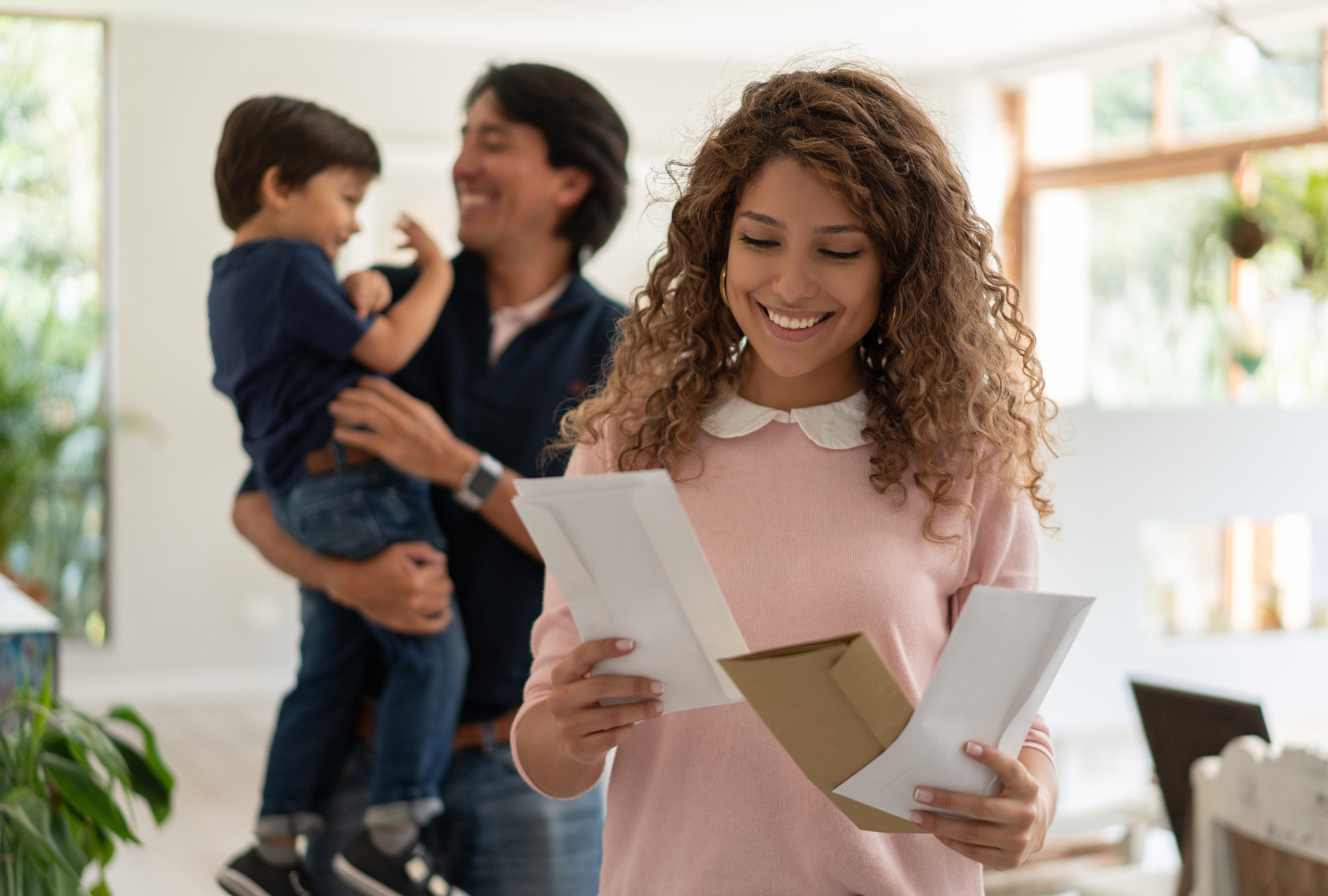 Woman looking happy to read a letter with man and child in the background