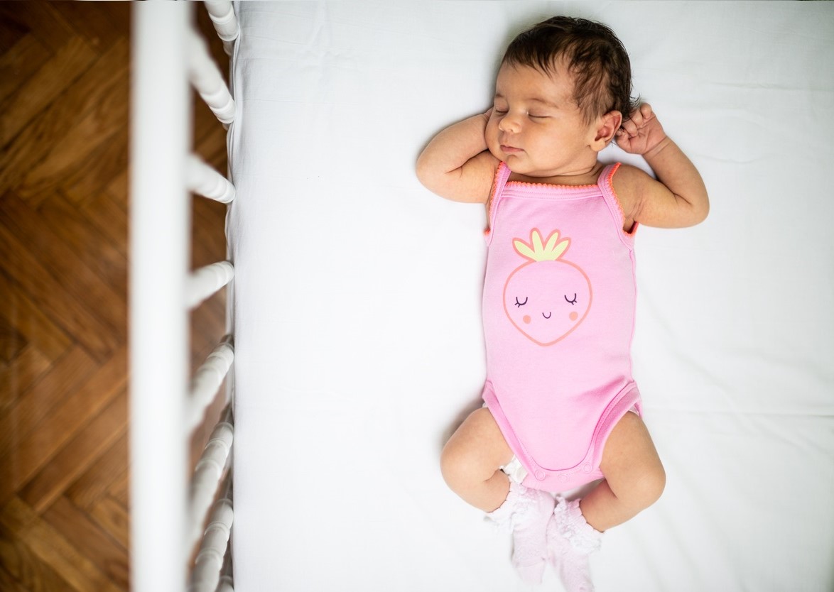 Baby in pink onesie sleeping on its back